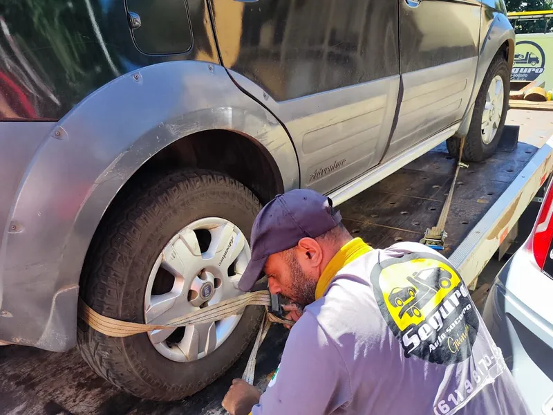 Técnico do Seguro Auto Socorro prendendo a cinta na roda de um utilitário sobre a plataforma do guincho
