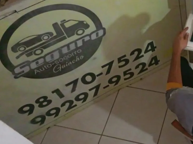 Atendente do Seguro Auto Socorro Guincho na central da empresa, ao lado da placa com os telefones de plantão
